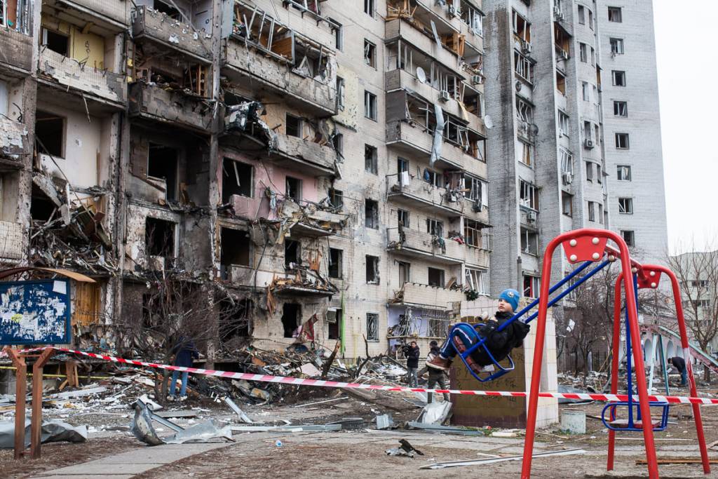 Киев. Мальчик на детской площадке около разрушенной обстрелом многоэтажки. Автор фото Владимир Петров