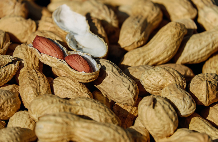 Плоды арахиса сложены в кучу, один из них вскрыт и в нем видны семена.