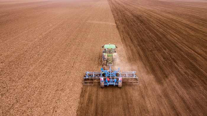 Трактор с культиватором проводит весеннюю обработку почвы в поле.