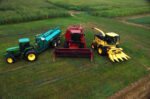 Зеленый трактор и красный и желтый комбайны стоят на зеленом поле.