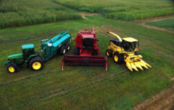 Зеленый трактор и красный и желтый комбайны стоят на зеленом поле.