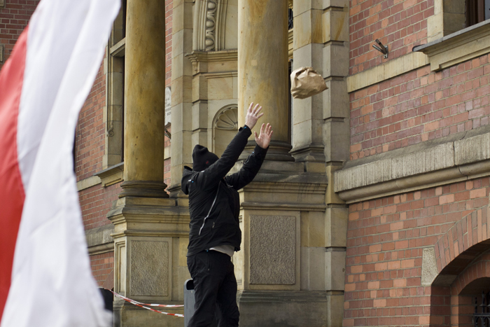 Человек в черной одежде забрасывает пакет в окно крипичного здания с колоннами.