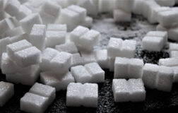 Кусочки белого сахара-рафинада лежат на черном столе.