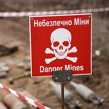 Червона табличка з написом "Небезпечно, міни" на українській і англійській мові.