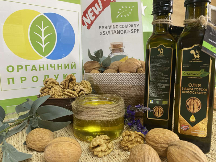 Бутылки и баночка с органическим ореховым маслом и грецкие орехи на фоне украинского логотипа "Органический продукт".