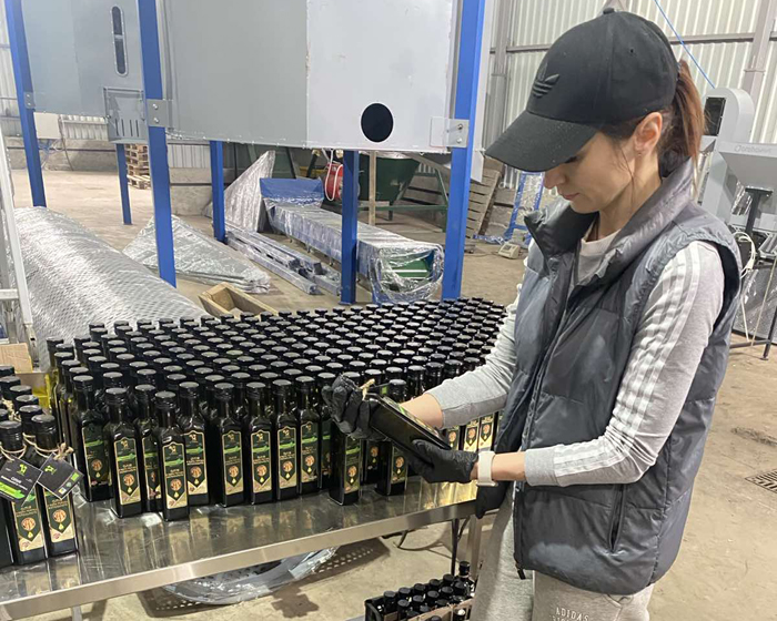 Работница держит бутылку органического орехового масла в перерабатывающем цеху.
