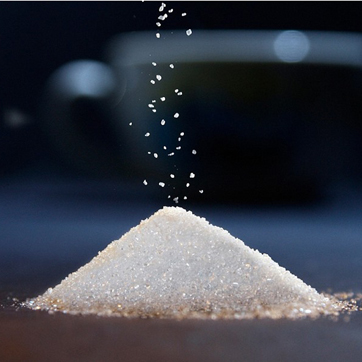 Гірка цукру на столі, на яку сиплеться ще цукор.