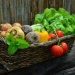 У плетеному кошику лежать цибуля, буряки, солодкий перець, салат і томати.